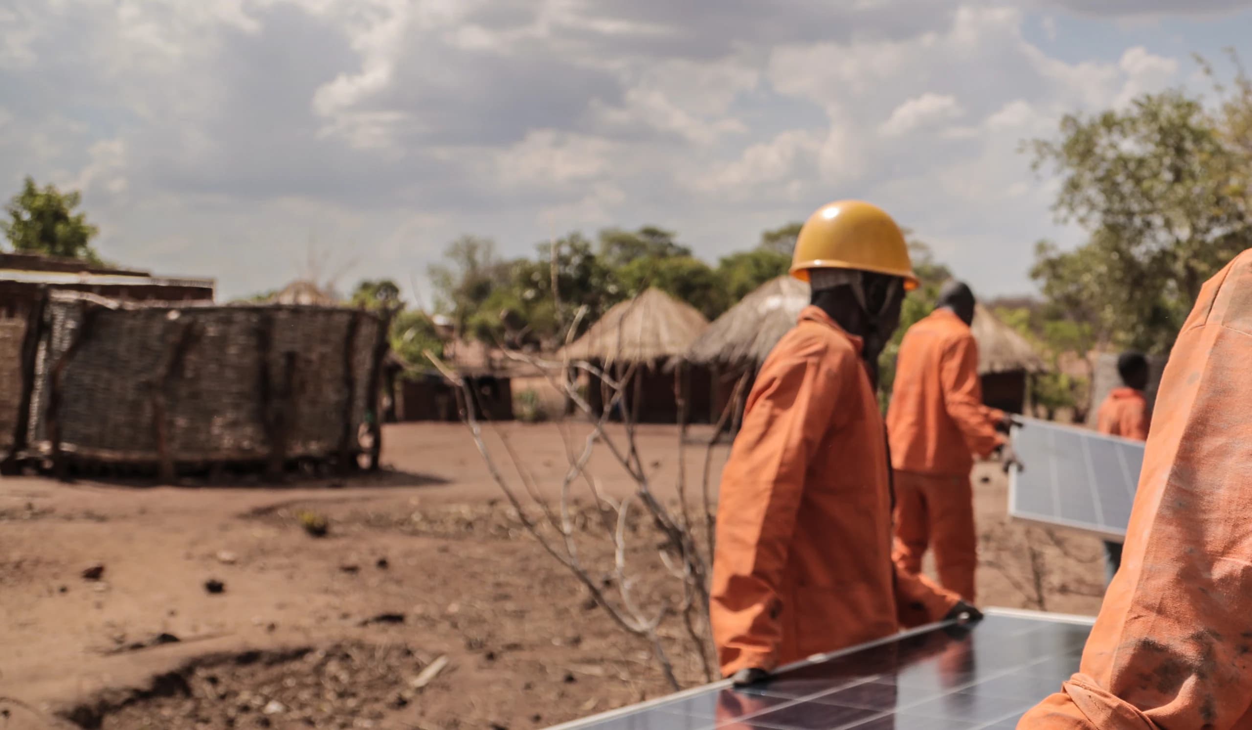 Solar technicians carrying photovoltaic panels through a rural African community